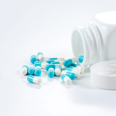 blue-white-capsules-pills-pouring-from-bottle-white-background-scaled.jpg